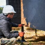 Male painter using paint roller, doing exterior paint work while building wooden frame house.