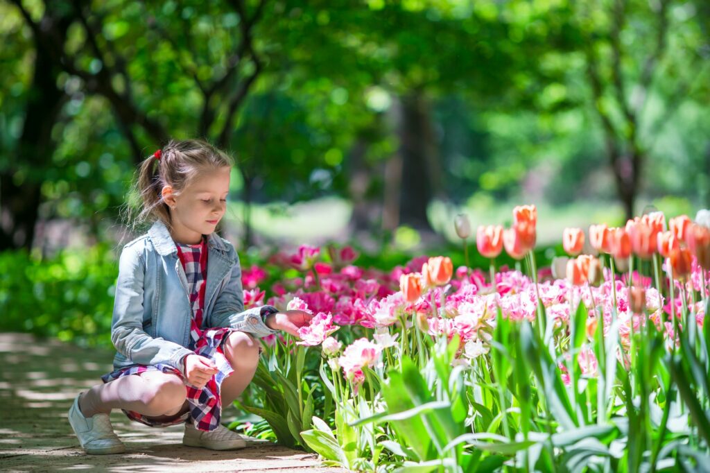 Little adorable girl with flowers in tulips garden